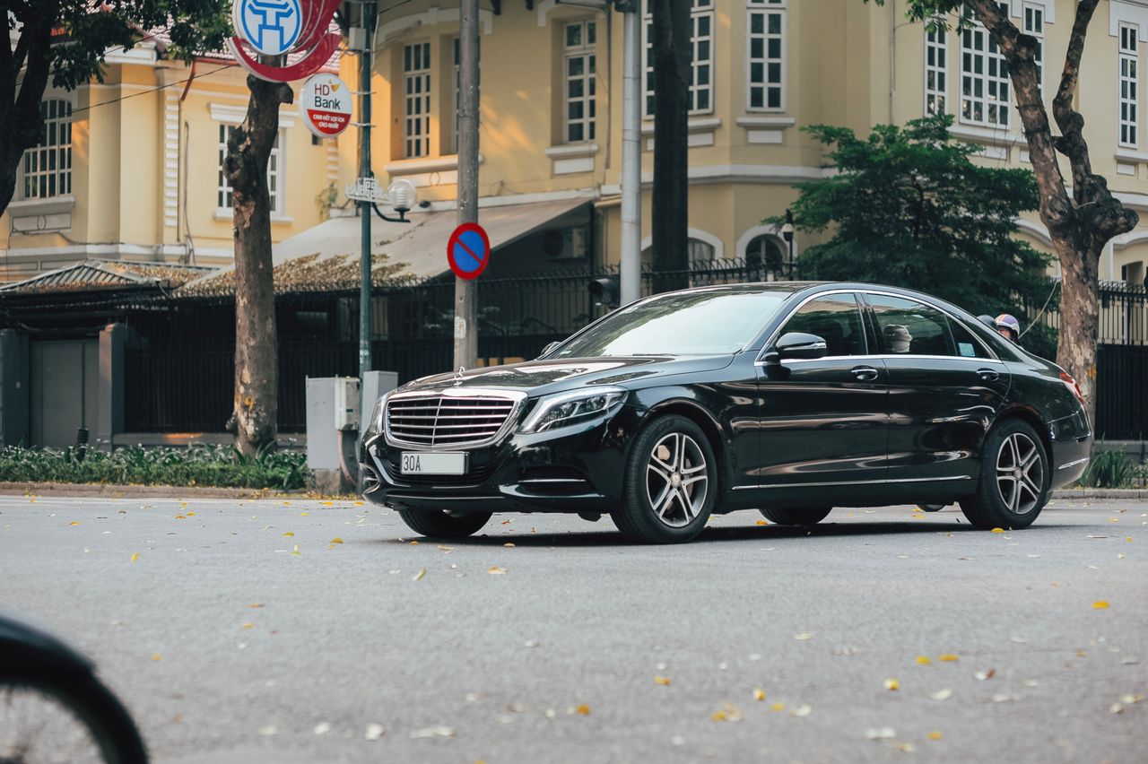 services-04 A sleek black sedan navigates an urban street lined with historic buildings and lush trees.