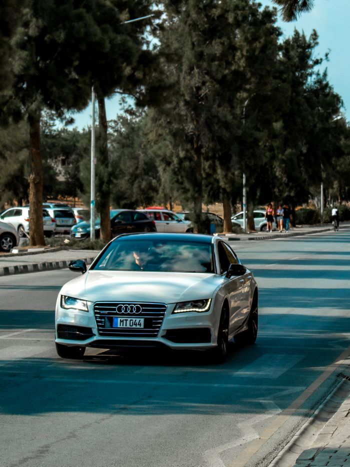 A sleek Audi car driving down a tree-lined street on a sunny day, showcasing luxury and style.